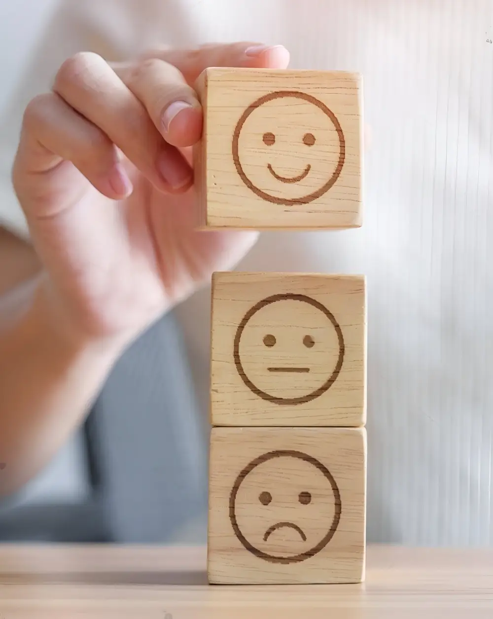 Mano sosteniendo bloques de madera con diferentes expresiones faciales para representar feedback de satisfacción del cliente